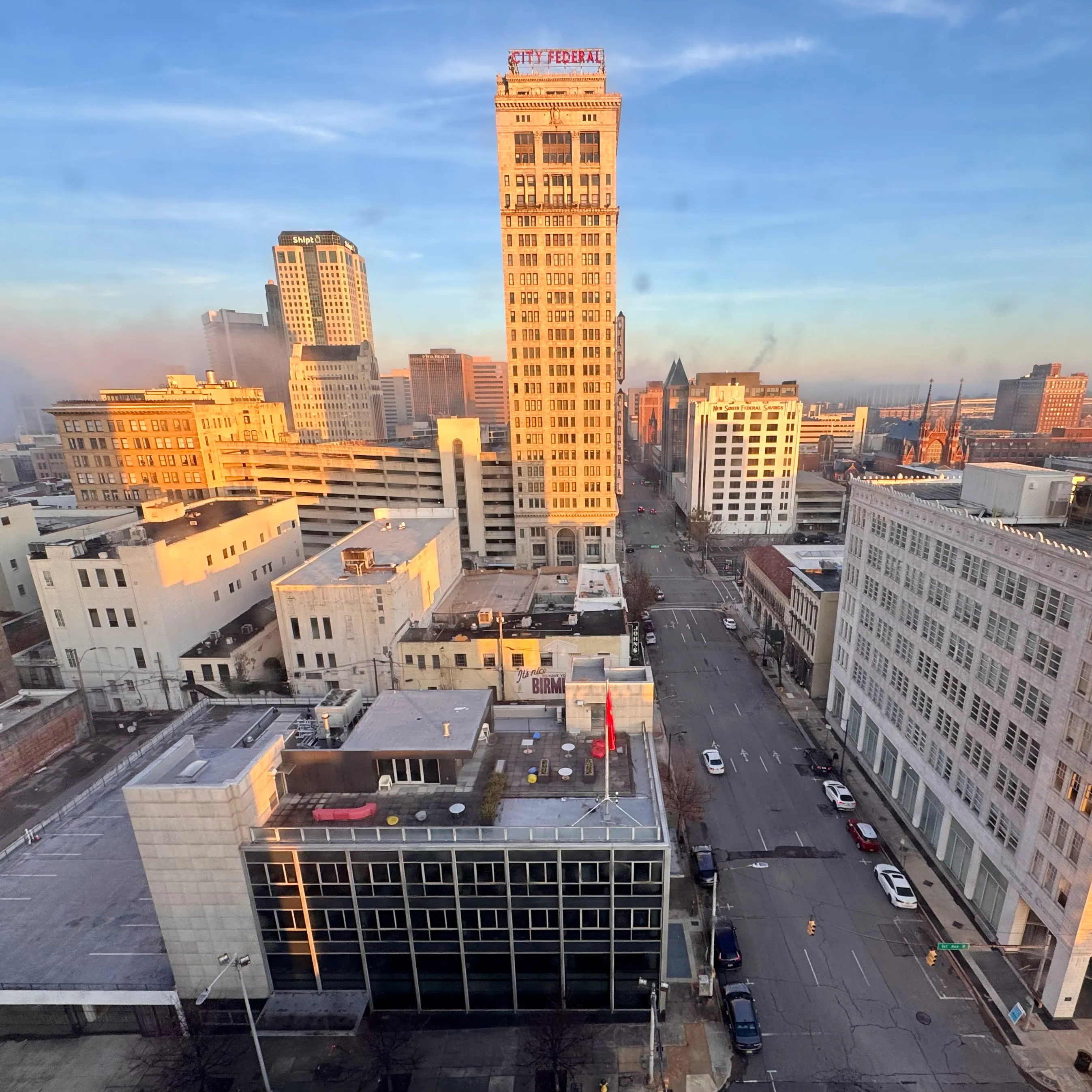 Downtown Birmingham at golden hour seen from a high window, the City Federal tower rising above quiet streets.