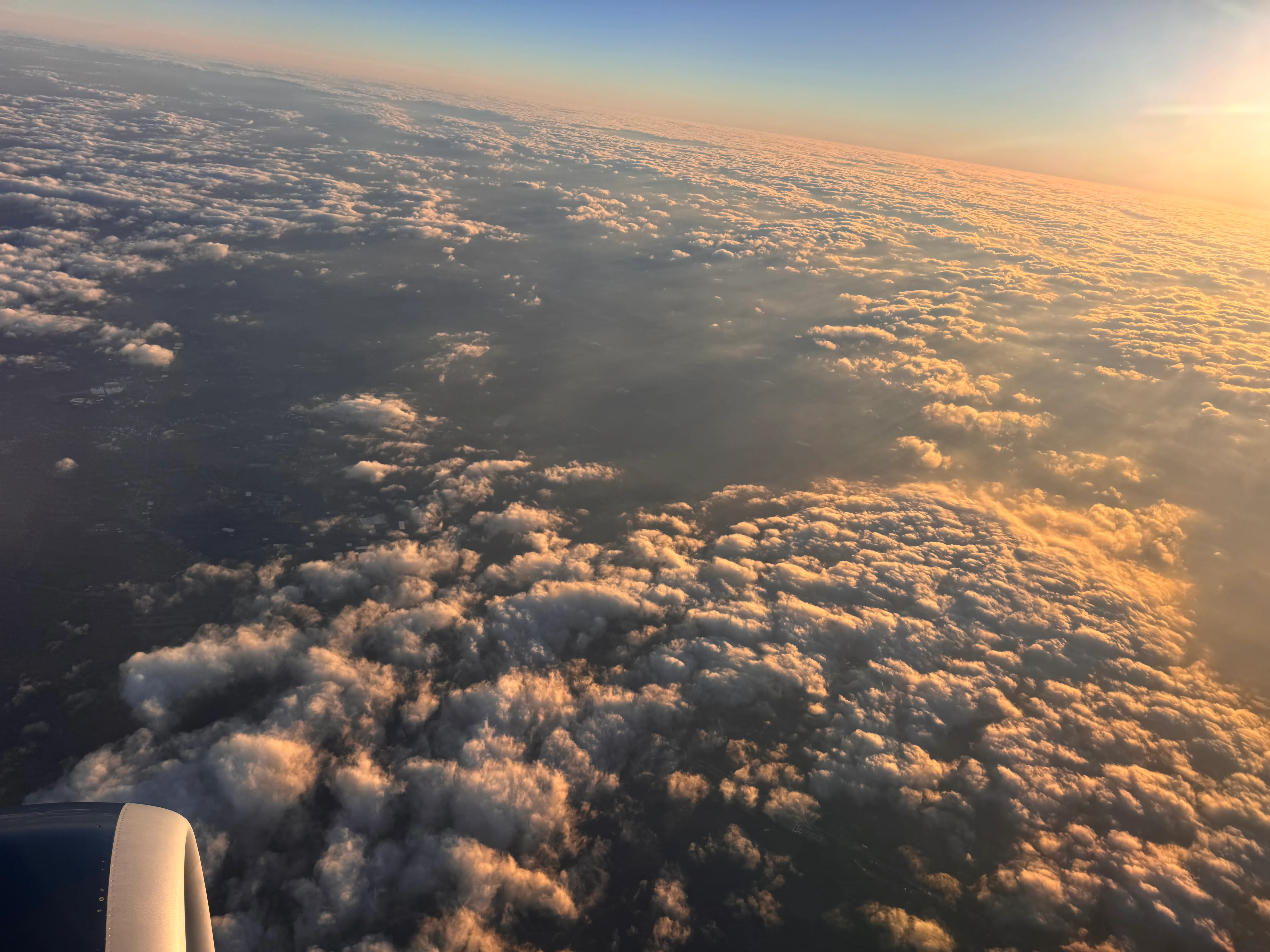 The view from an airplane window of clouds lit gold by a low sun, with the engine cowling visible at the corner.