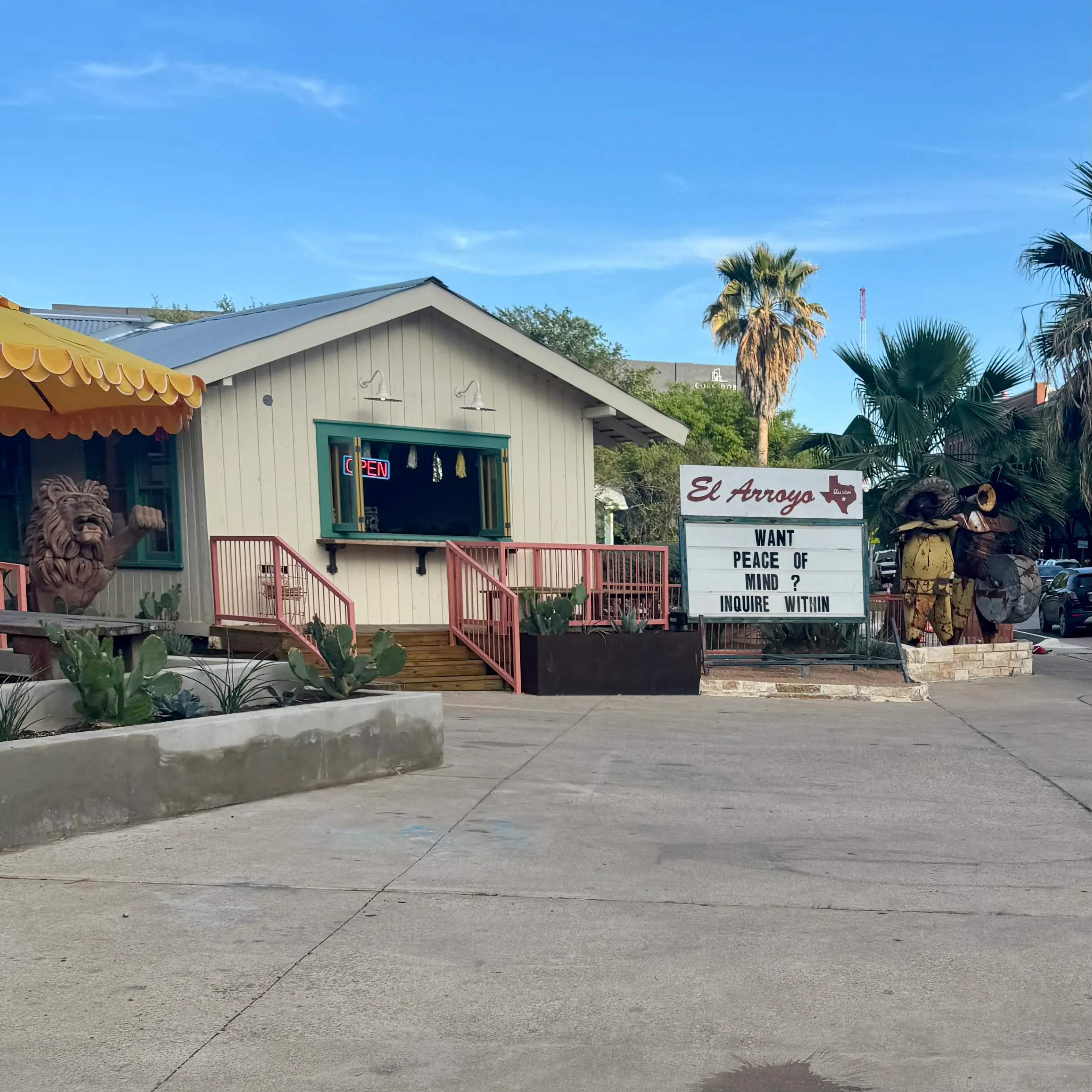 The El Arroyo restaurant in Austin, its marquee sign reading "Want peace of mind? Inquire within" beside a cottage with a yellow awning and palm trees.
